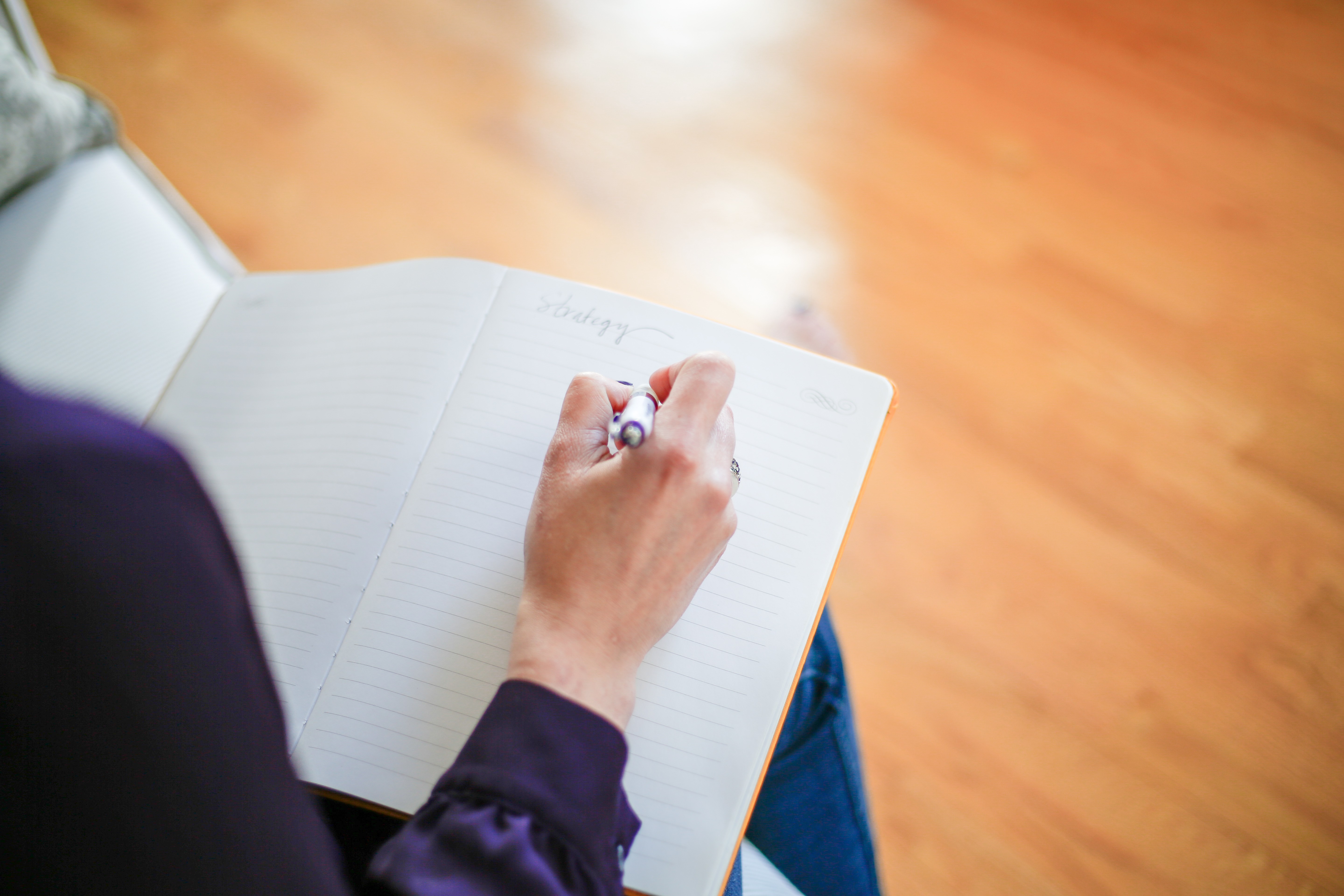 Woman writing in a notebook while sitting on light wooden flooring.