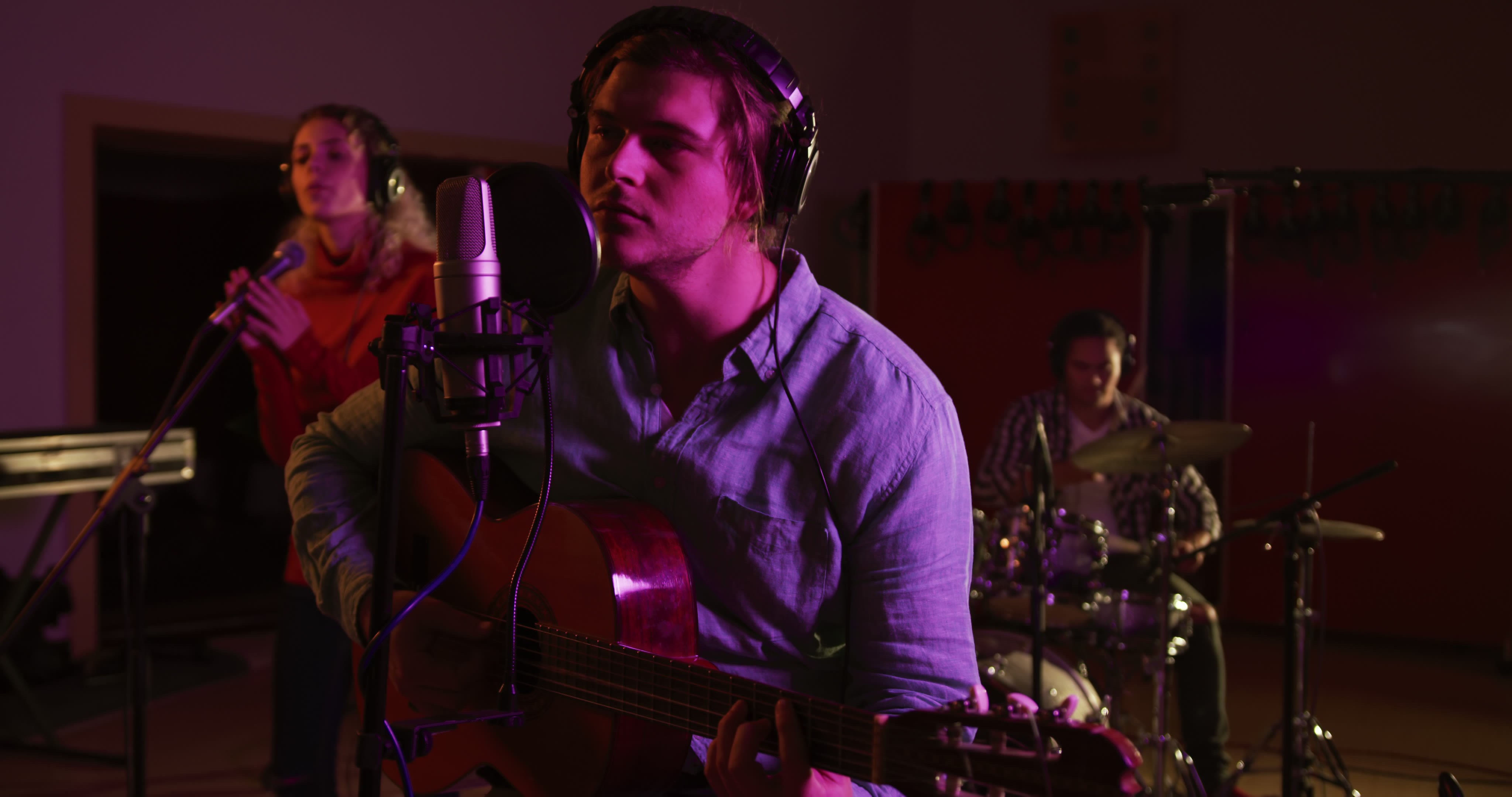 A music band of three members is collaborating during a recording session. The male guitarist is leading the performance, while a female vocalist is providing backup and a male drummer sets the rhythm. From pikwizard.com