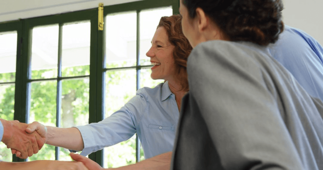 Business professionals smiling and shaking hands in a casual restaurant environment. 