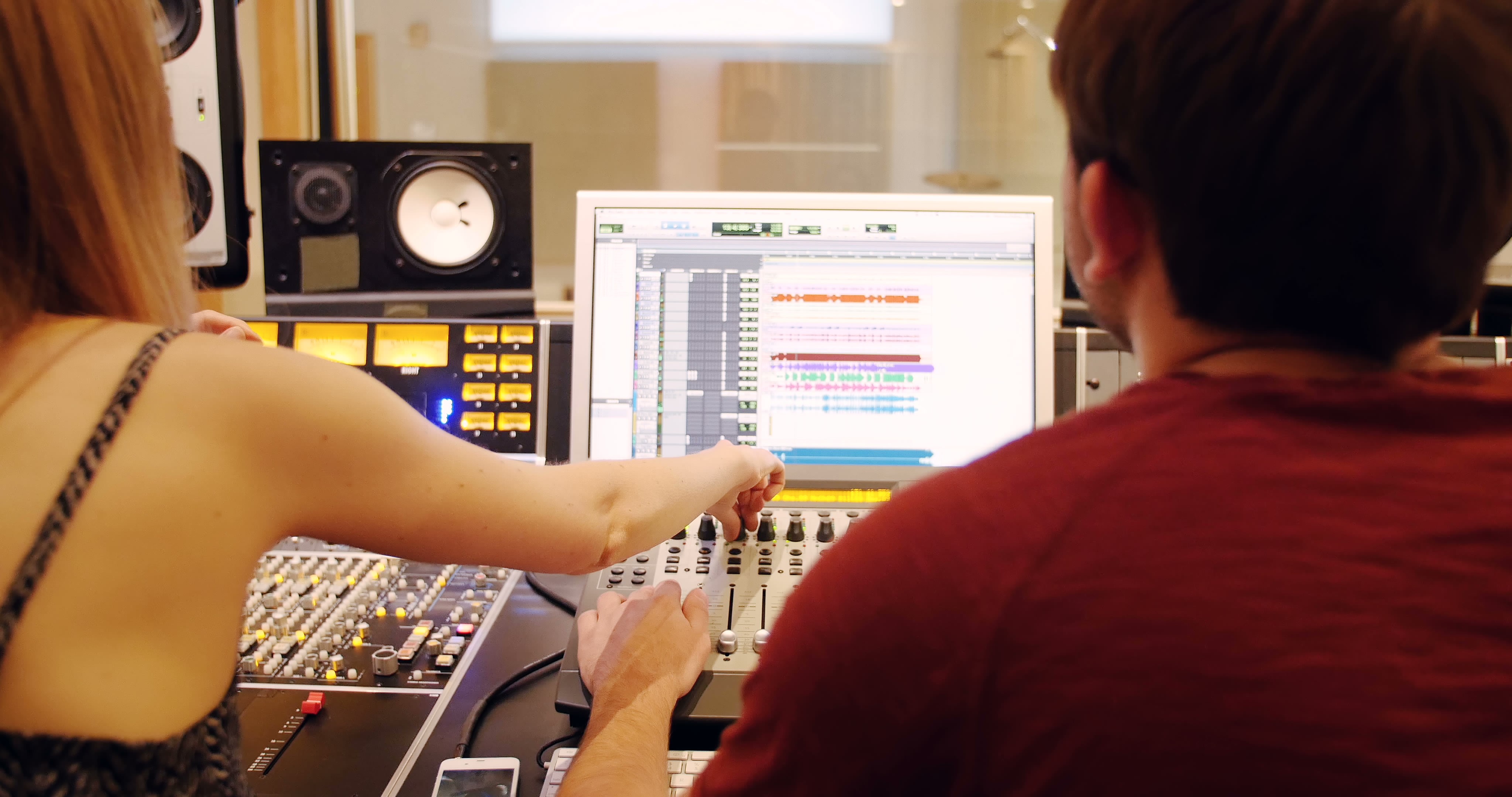 Two audio professionals are working together in a recording studio, focusing on sound mixing using advanced technology.